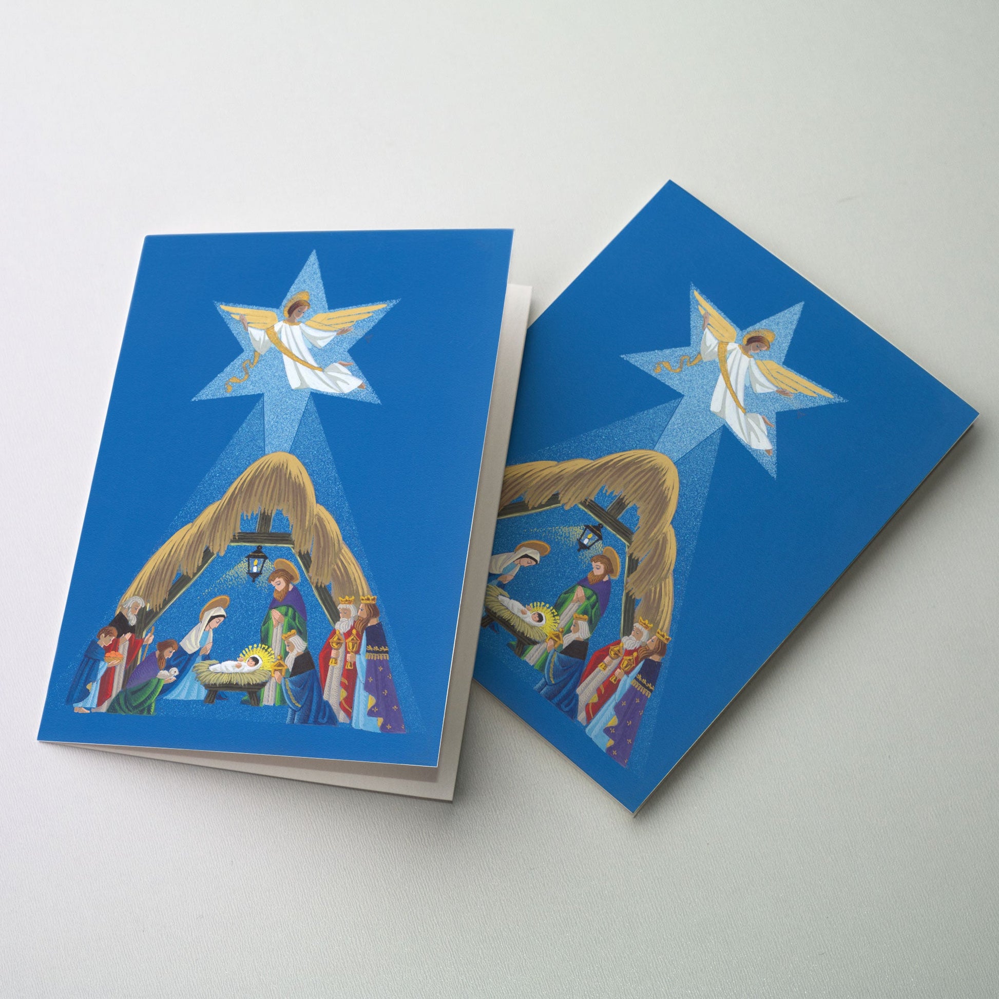 An exquisitely illustrated nativity by Philippe Cloes on a background of deep blue. An angel is seen above in the midst of a star-shaped glow which encompasses the entire nativity.