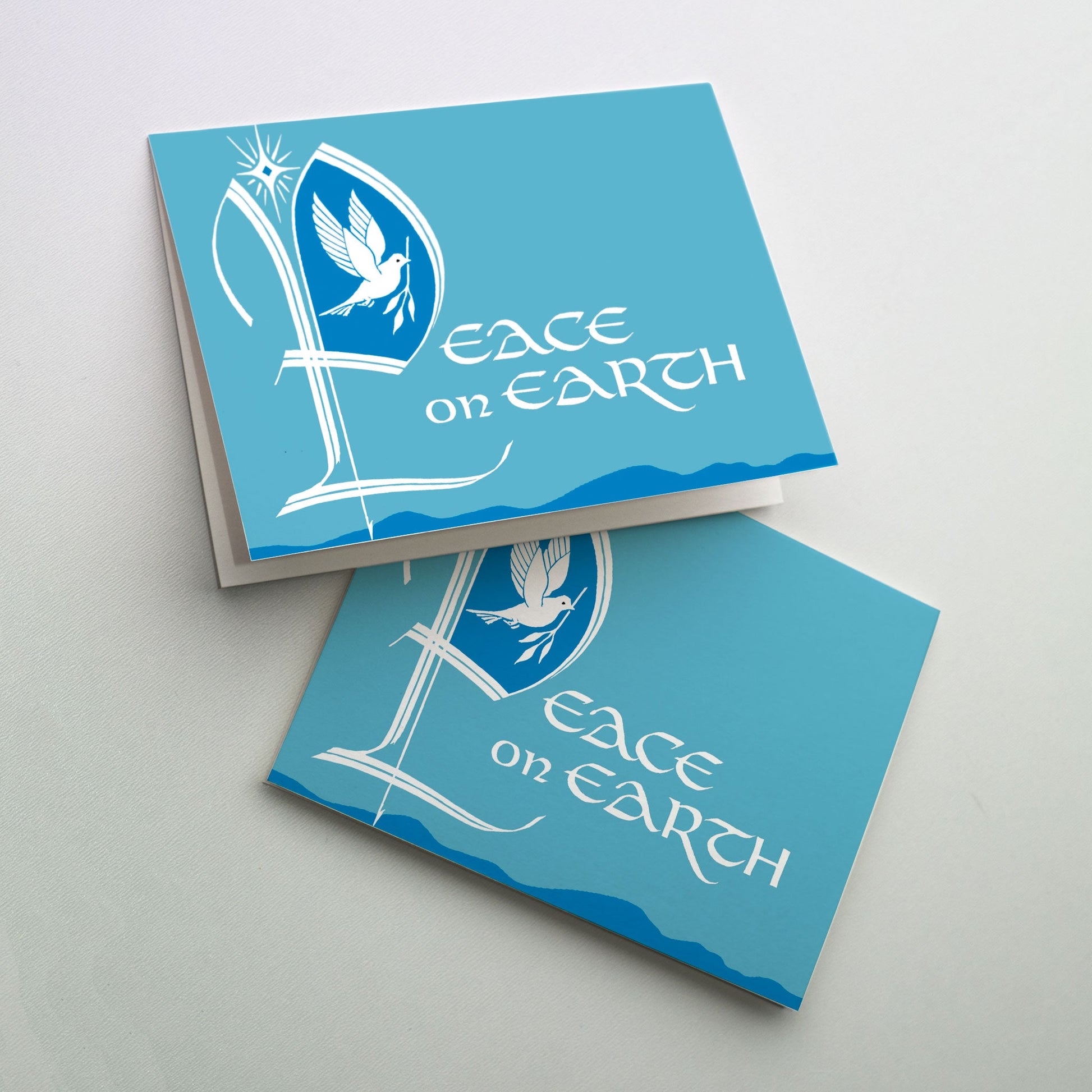 A white dove with olive branch inside a large start letter &quot;P&quot; for the word &quot;Peace&quot; of &quot;Peace on Earth&quot;. The background in a light teal color with dark blue mountains and hills visible at the bottom of the card. A bright star is above the initial letter.