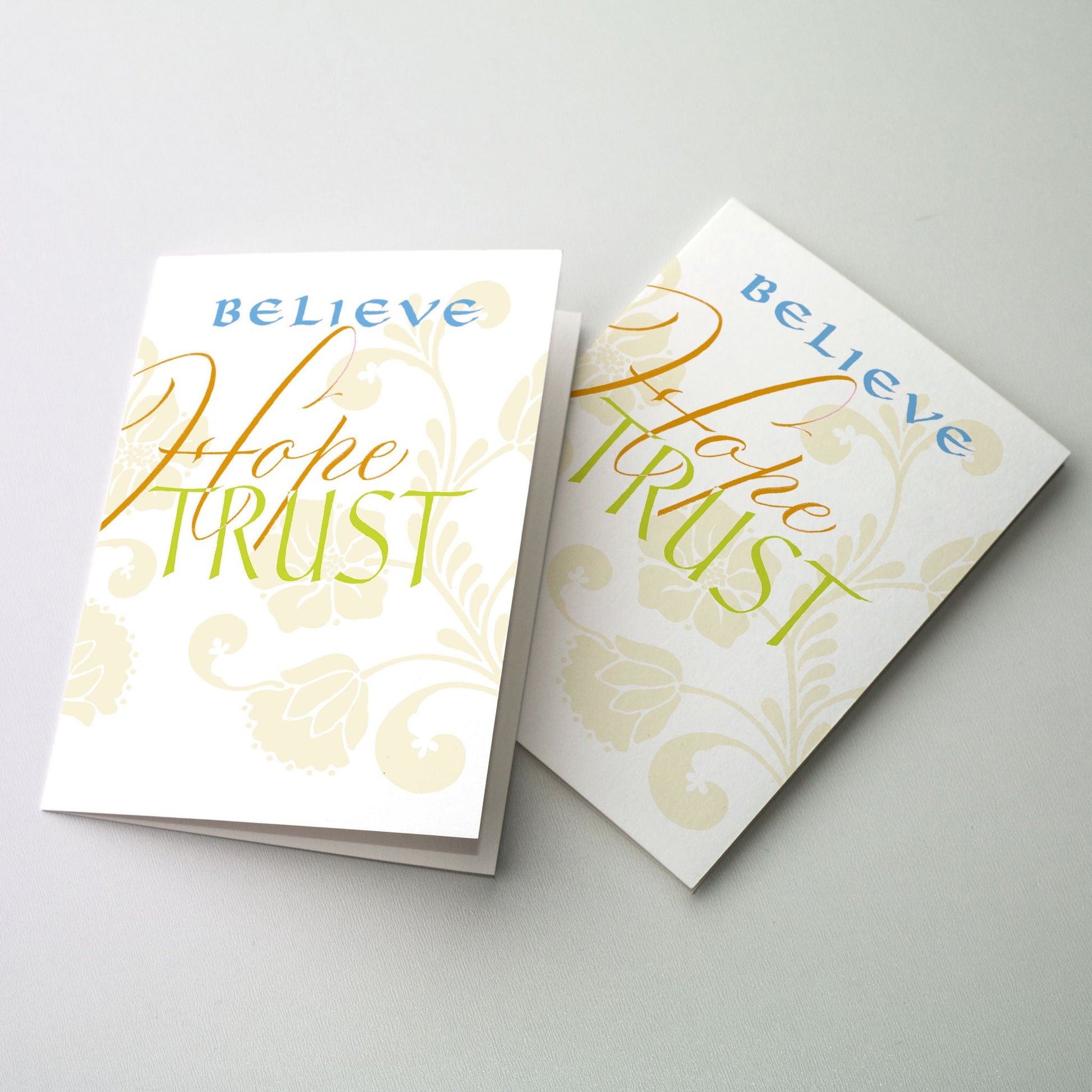 <br>&quot;Believe, Hope, Trust&quot; in blue, deep gold and chartreuse on white ground with light green floral pattern in background.