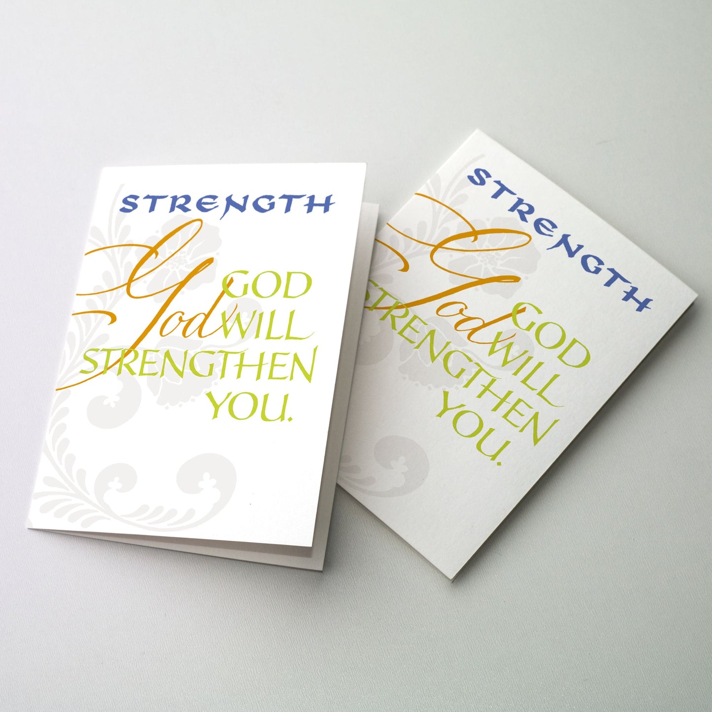 <br> &quot;God will strengthen you&quot; in blue, deep gold and chartreuse on a white ground with gray floral pattern in background.